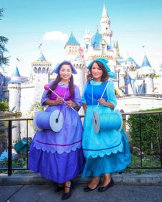 two girls dressed in costumes standing next to each other near a castle with blue turrets