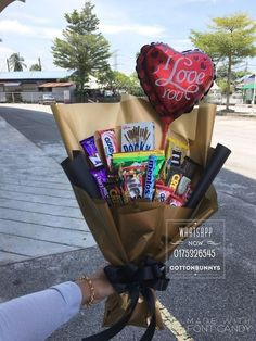 someone is holding a valentine's day bouquet with chocolates, candy and heart - shaped balloon