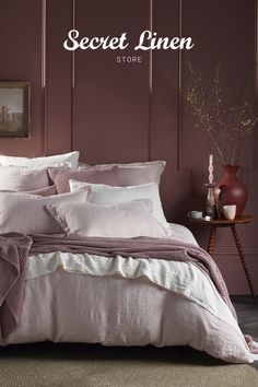 a bed with pink sheets and pillows in front of a wall painted maroon by farrow