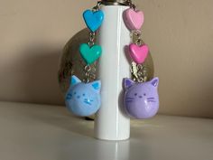 three cat shaped key chains are hanging from a white holder on a table next to a rock