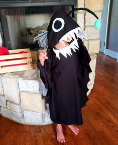 a person in a costume standing next to a fire place with a fake shark head on it's face