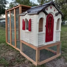 a chicken coop with a red door and window on the outside, in a yard