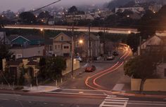 a city street at night with cars driving on it and houses in the background,