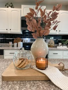 a kitchen counter top with a vase filled with leaves and cookies on it next to a candle