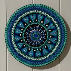 a blue and green plate hanging on the side of a white wall with bead work