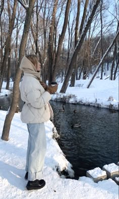 a person standing in the snow next to a river and trees with no leaves on them