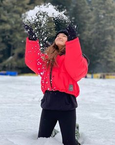 a woman in red jacket throwing snow into the air on top of snow covered ground