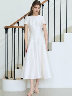 a woman in a white dress standing next to a stair case and handrails