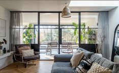 a living room filled with furniture and lots of windows next to a wooden floor covered in plants