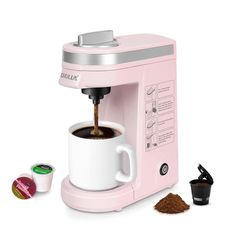 a pink coffee maker with two cups next to it on a white surface and one cup is being filled with ground coffee