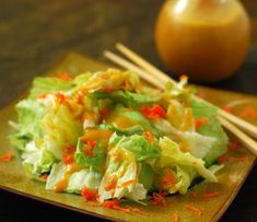 a wooden plate topped with lettuce and carrots next to chopsticks