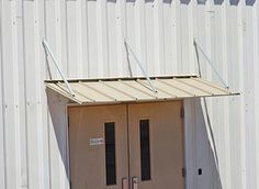 two double doors are open in front of a white building with metal bars on the roof