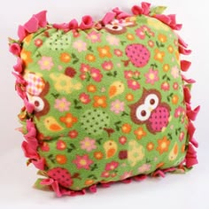 a green pillow with pink ruffles and an owl design on the front, sitting on a white surface