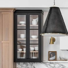 a kitchen with marble counter tops and wooden cabinets, black pendant light hanging from the ceiling