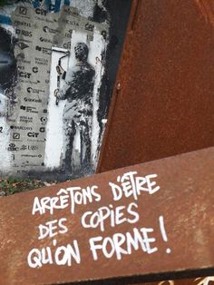 graffiti written on the side of a building near a street sign that reads, arretons deie des copies quion forme