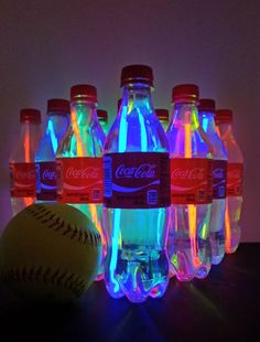 six coca - cola bottles with neon lights and a baseball on the table next to them