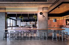 an open kitchen and dining area with bar stools in the foreground, surrounded by concrete walls