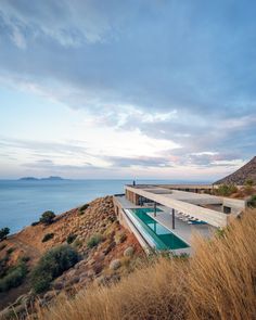 an outdoor swimming pool on the side of a cliff overlooking the ocean and hills with grass growing in front of it