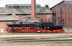 a black and red train is on the tracks in front of an old brick building