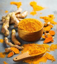 tumerical powder in a wooden bowl next to fresh tumerica roots and ginger