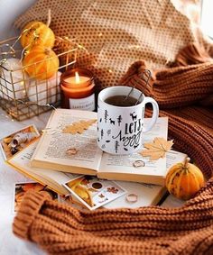 an open book and cup of coffee on a bed with pumpkins, candles and blankets