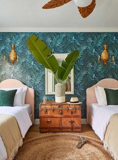 two beds in a room with blue and green wallpaper, one has a trunk on the floor