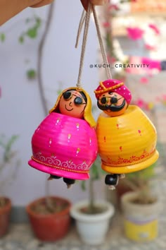 two small dolls hanging from strings in front of potted plants