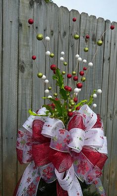 a red and white bow on top of a vase filled with flowers next to a fence