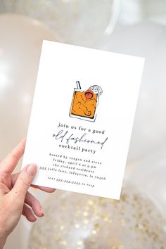 a hand holding up a card with an orange cocktail on it and balloons in the background