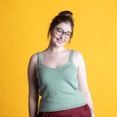 a woman with glasses standing in front of a yellow background wearing a green tank top