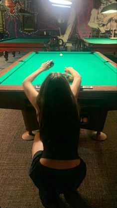 a woman sitting at a pool table in front of a light