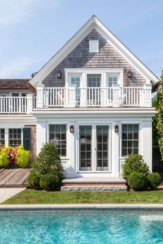 a house with a pool in front of it and some bushes on the lawn next to it