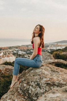 a woman sitting on top of a large rock next to the ocean with her eyes closed