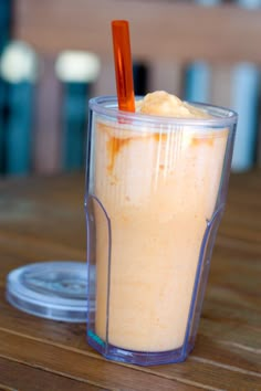 a drink in a plastic cup with an orange straw sticking out of it on top of a wooden table