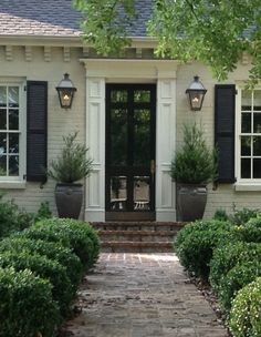 a white house with black shutters and two potted plants on the front steps