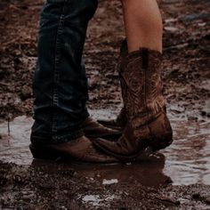 two people standing in the mud wearing cowboy boots