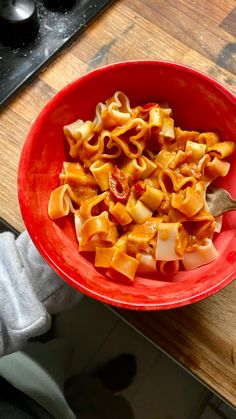 a red bowl filled with pasta on top of a wooden table next to a stove