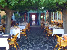 an outdoor dining area with yellow chairs and tables covered in white tablecloths under trees