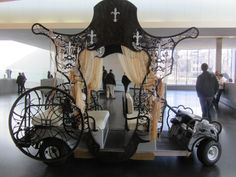 an elaborately designed carriage is in the middle of a room with people walking around