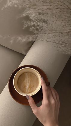 a person holding a cup of coffee on top of a saucer with water in the background