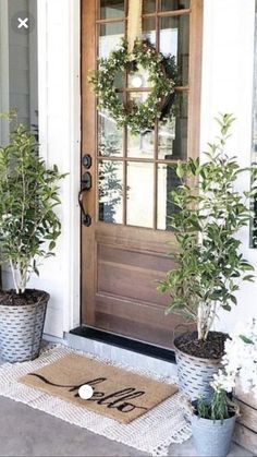 two potted plants are sitting on the front porch with a welcome mat and wreath