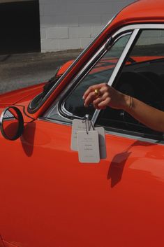 an orange car with a tag on the front window and a person's hand in the driver's seat