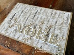 a card with the word noel written in white and gold on top of a wooden table