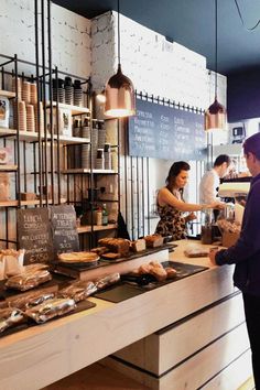 people are standing in front of the counter at a coffee shop with food on it