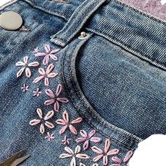 a pair of blue jeans with pink flowers on the side and silver buttons in the back