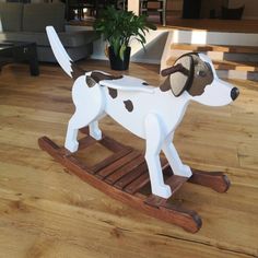 a white and brown dog sitting on top of a wooden sled next to a potted plant