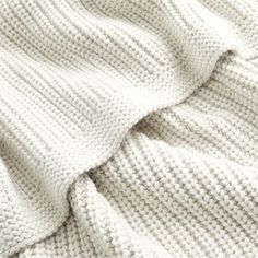 a white knitted blanket laying on top of a bed