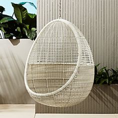 the hanging chair is made out of wicker and has a plant in front of it