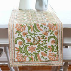 an orange and green table runner sitting on top of a white table next to a vase