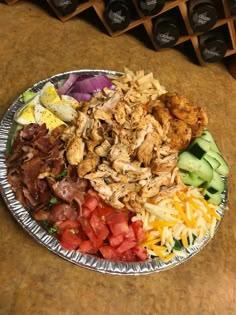 a metal plate filled with lots of food on top of a wooden table next to wine bottles